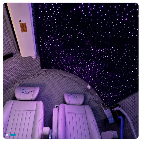 Chamber interior lit in purple, showing the fiber-optic starlight ceiling glowing with violet stars above quilted padded walls and two light leather Oxygen Health Systems seats with headrests